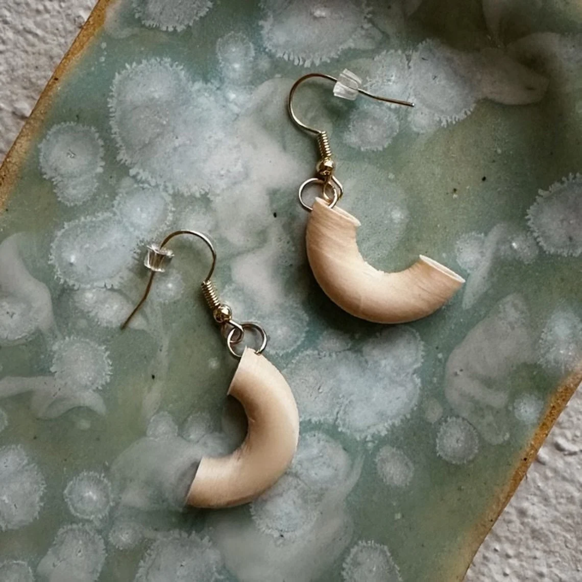 Pair of 3D-printed macaroni earrings on a speckled sage-green ceramic dish.