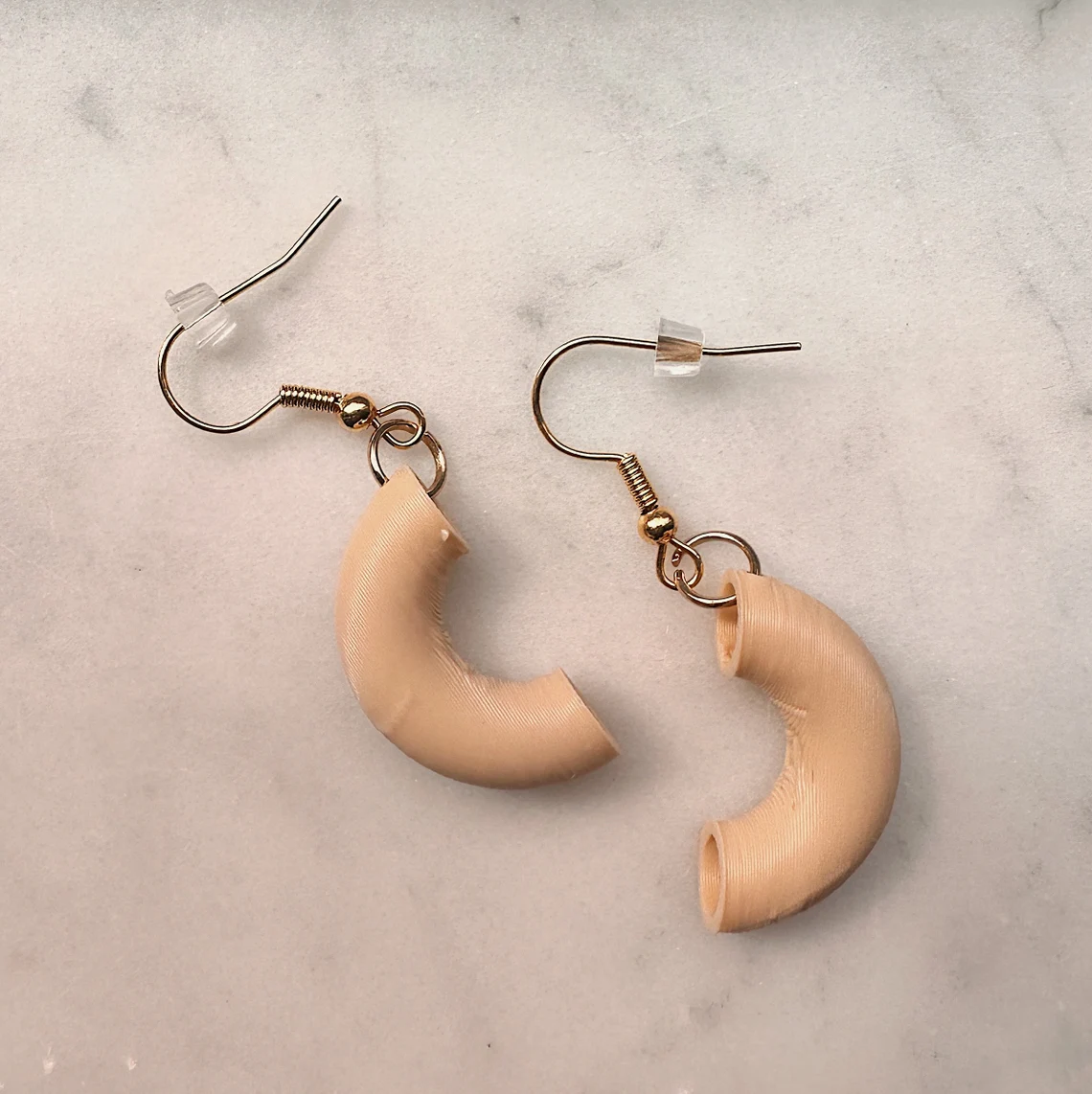 Close-up of the macaroni earrings on white marble, angled to show the hollow tube opening and ridged print texture.