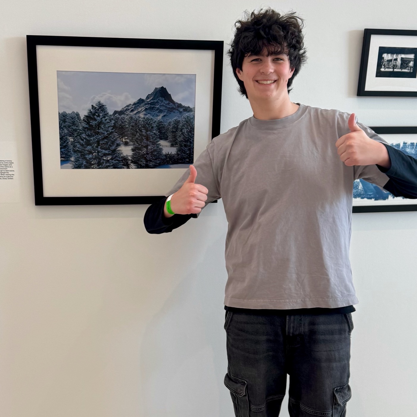 Emmet Cohen smiling and giving two thumbs up in a gallery, standing next to his framed digital artwork "Frozen Peaks."