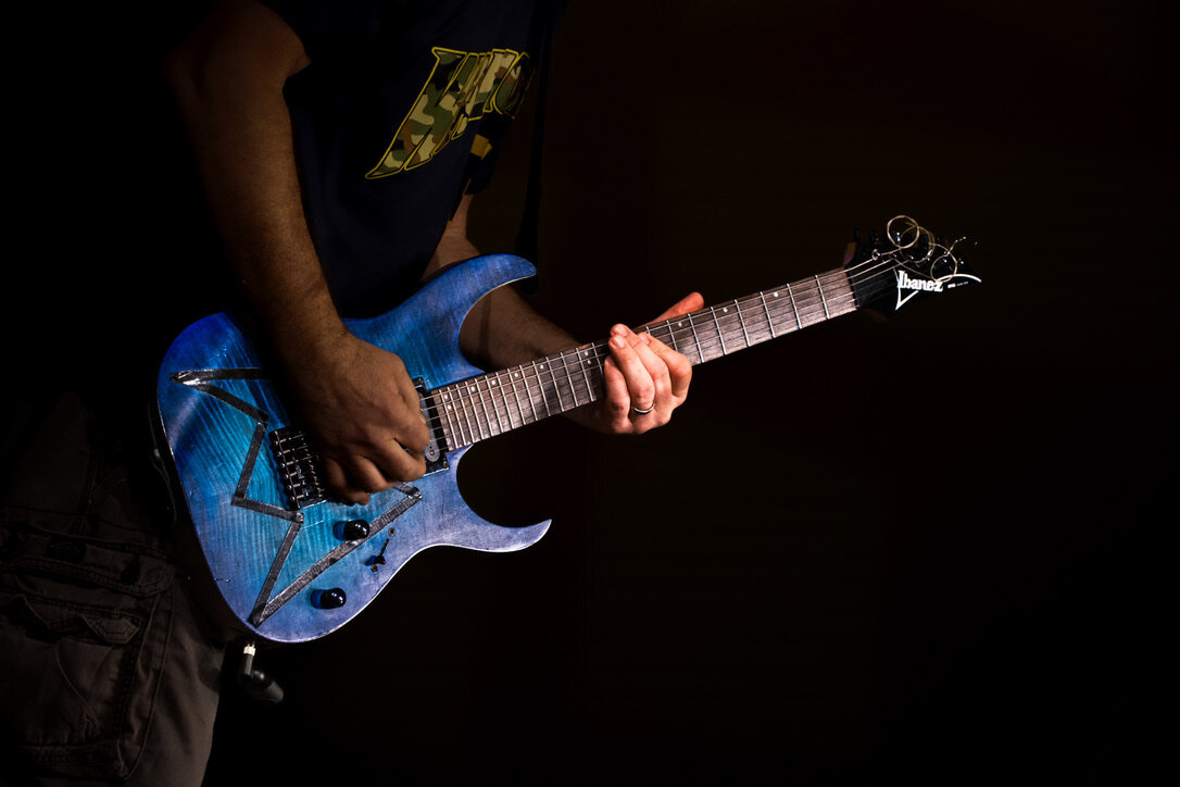 Close-up of hands playing a blue Ibanez electric guitar against a dark background