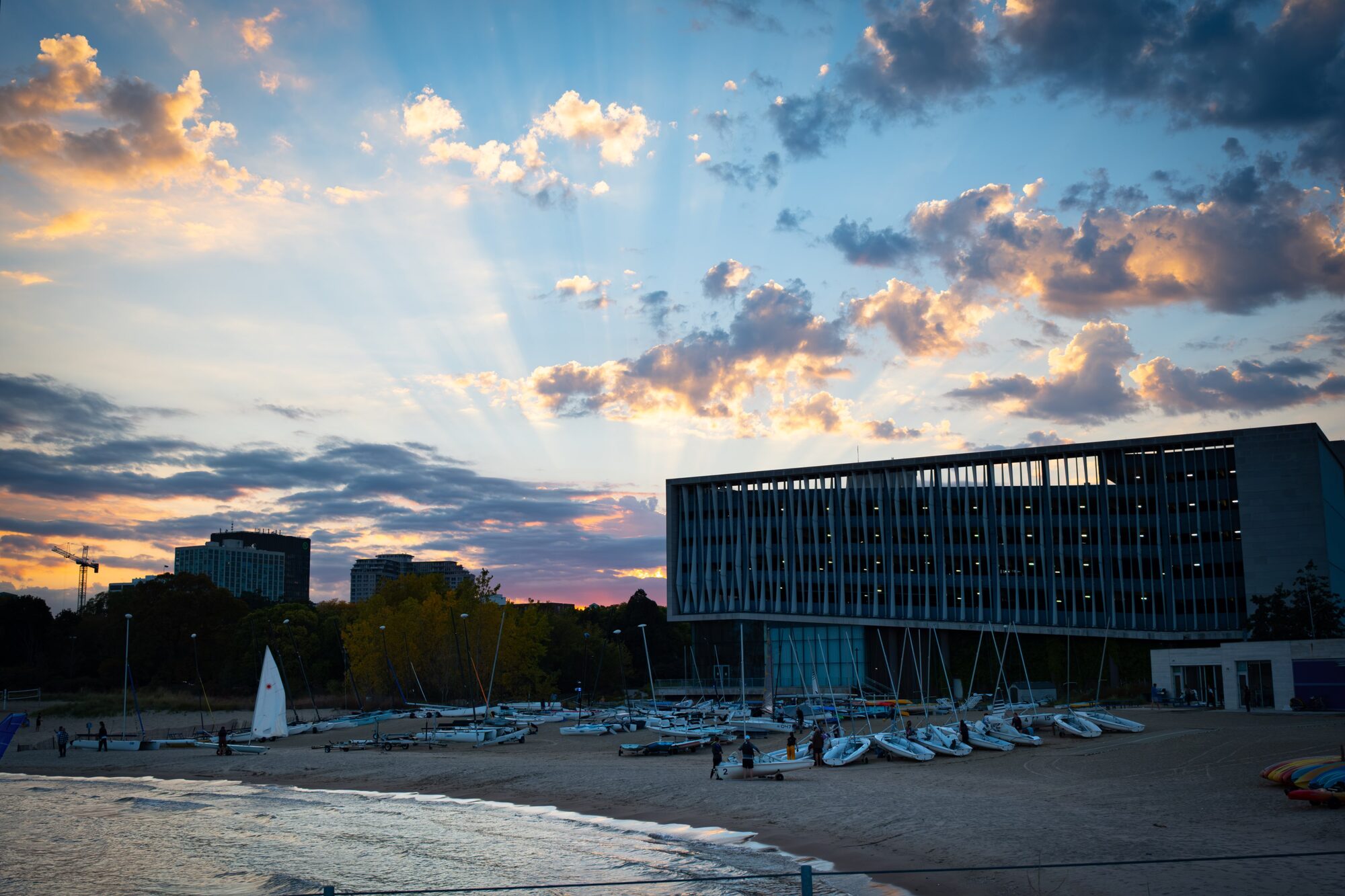 Sunrays breaking through clouds over a lakefront marina and a modern building at sunset
